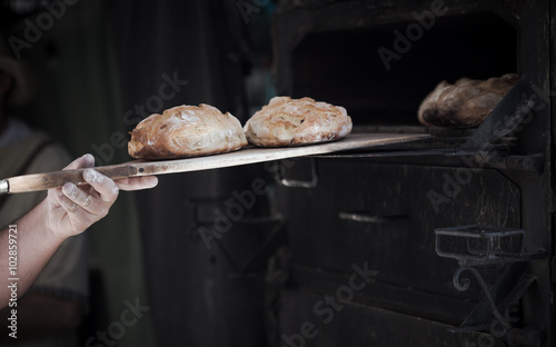 Close-up of a man baker introducing breads in a classic oven  