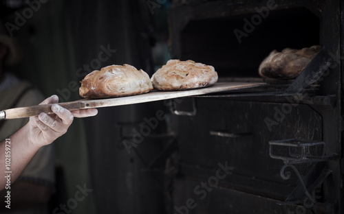 Close-up of a man baker introducing breads in a classic oven 