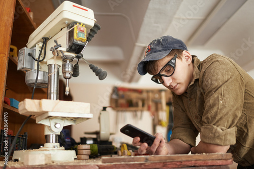 Worker in glasses near the machine drills to break looking at phone