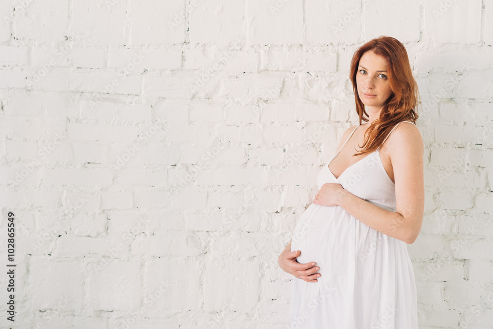 Pregnant woman in a white dress in a white brick wall