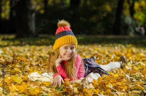 Pretty smiling girl lying on yellow leaves