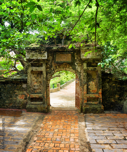 Brick walkway to old stone gate leading into tropical garden