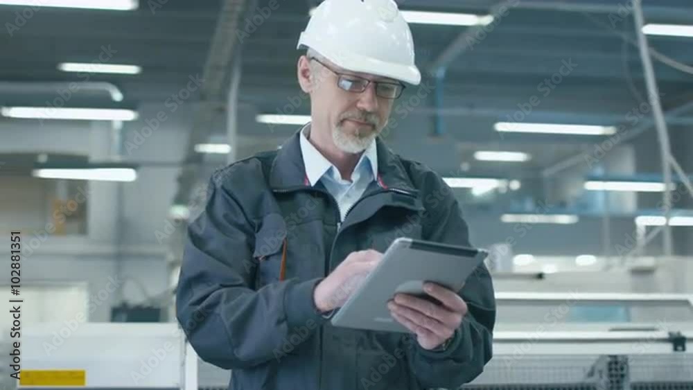Senior engineer in hardhat is using a tablet computer in a factory. Shot on RED Cinema Camera.