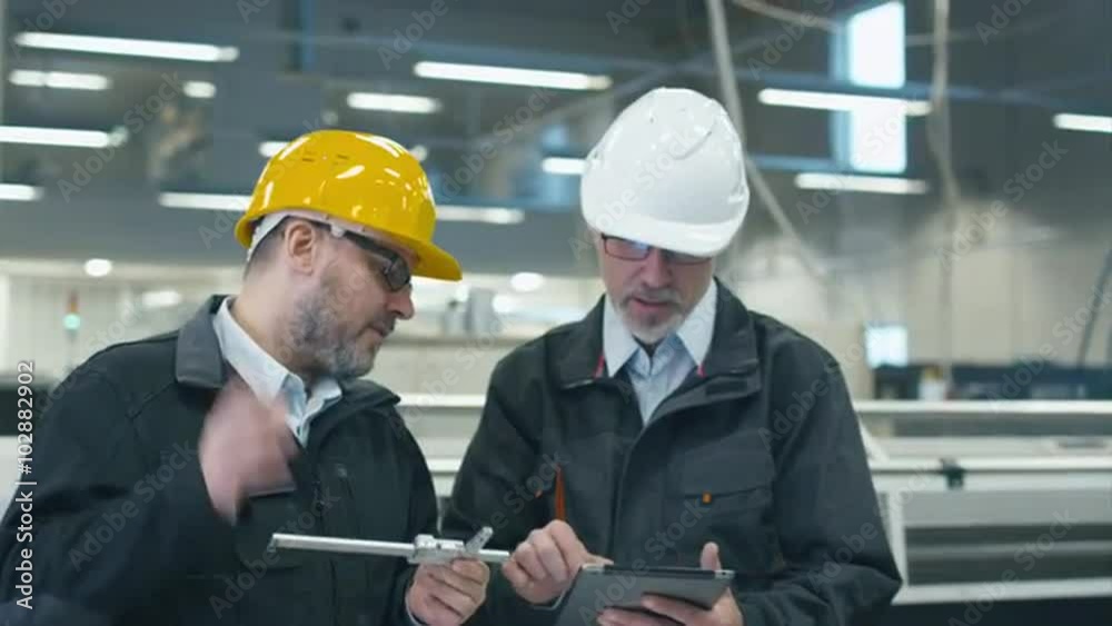 Two engineers discuss a blueprint while checking information on a tablet computer in a factory. Shot on RED Cinema Camera. Two engineers discuss a blueprint while checking information on a tablet computer in a factory. Shot on RED Cinema Camera.