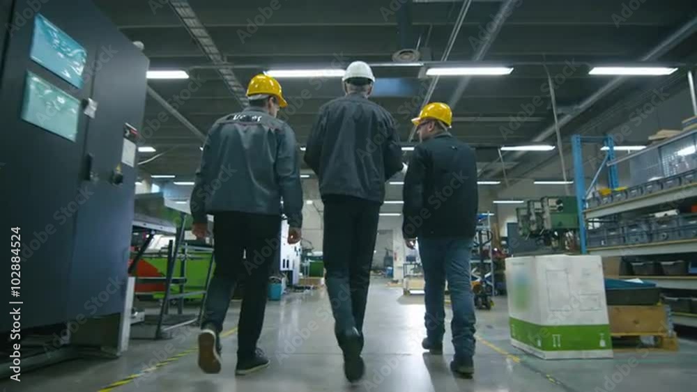 Back view of senior engineer and two workers are walking with papers through the factory space. Shot on RED Cinema Camera.