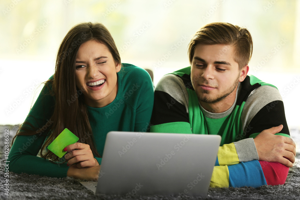 Young happy couple using credit card with laptop at home on light background Young happy couple using credit card with laptop at home on light background