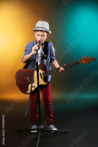 Little boy playing guitar and singing with microphone on a dark lighted background © Africa Studio