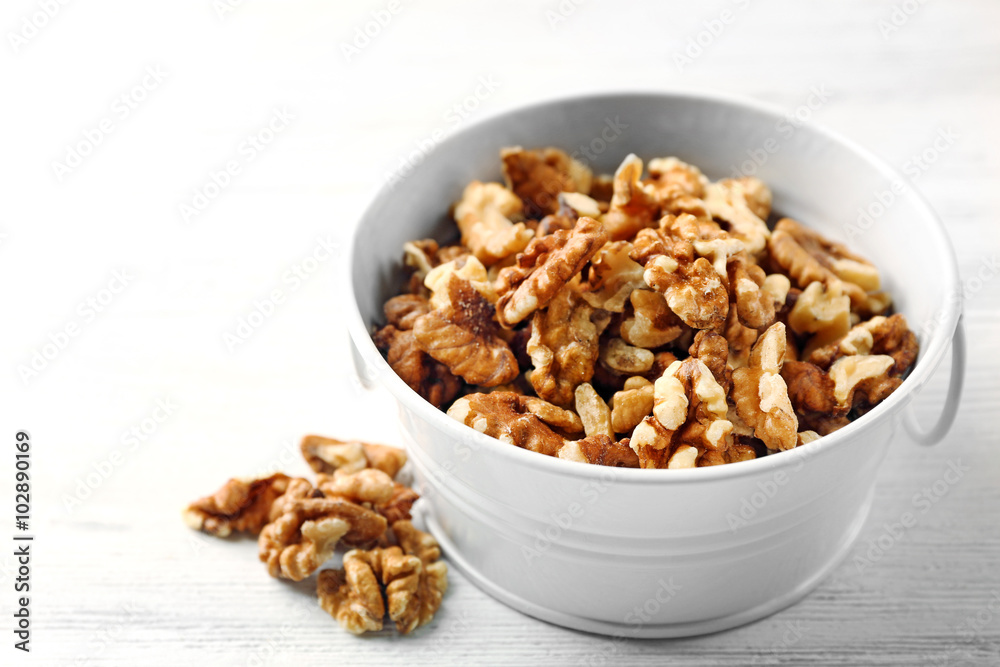 Walnut kernels in the metal bucket on white wooden background Walnut kernels in the metal bucket on white wooden background