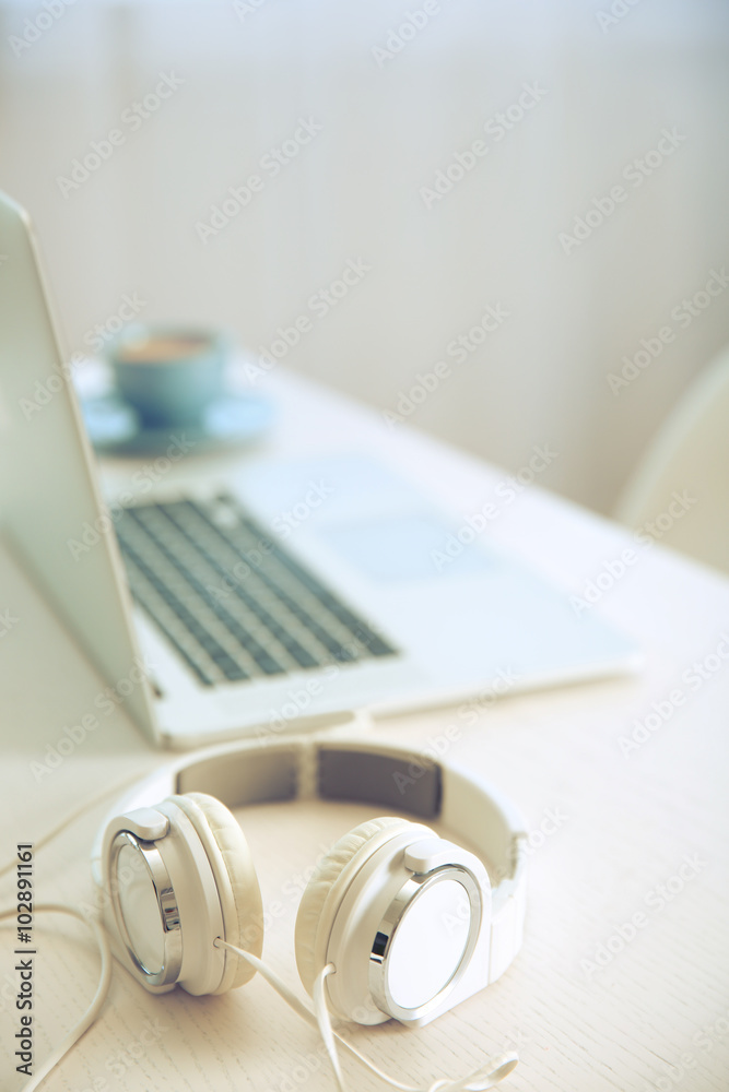 Headphones and laptop on white table against defocused background Headphones and laptop on white table against defocused background