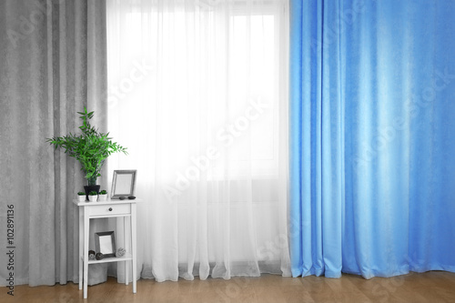 Small white table with green plant and frames on curtain background