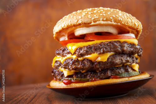 Cuadro en lienzo Big beef burger with three patties and cheese on plate , wood background