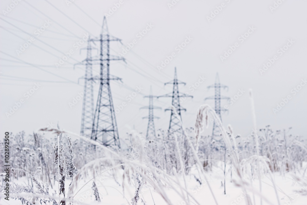 Electricity towers in winter. Blurred background, focus on dry snowy grass