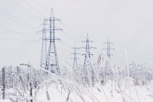 Electricity towers in winter. Blurred background, focus on dry snowy grass