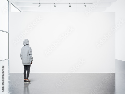 Young woman walking in modern gallery and looking at the blank canvas