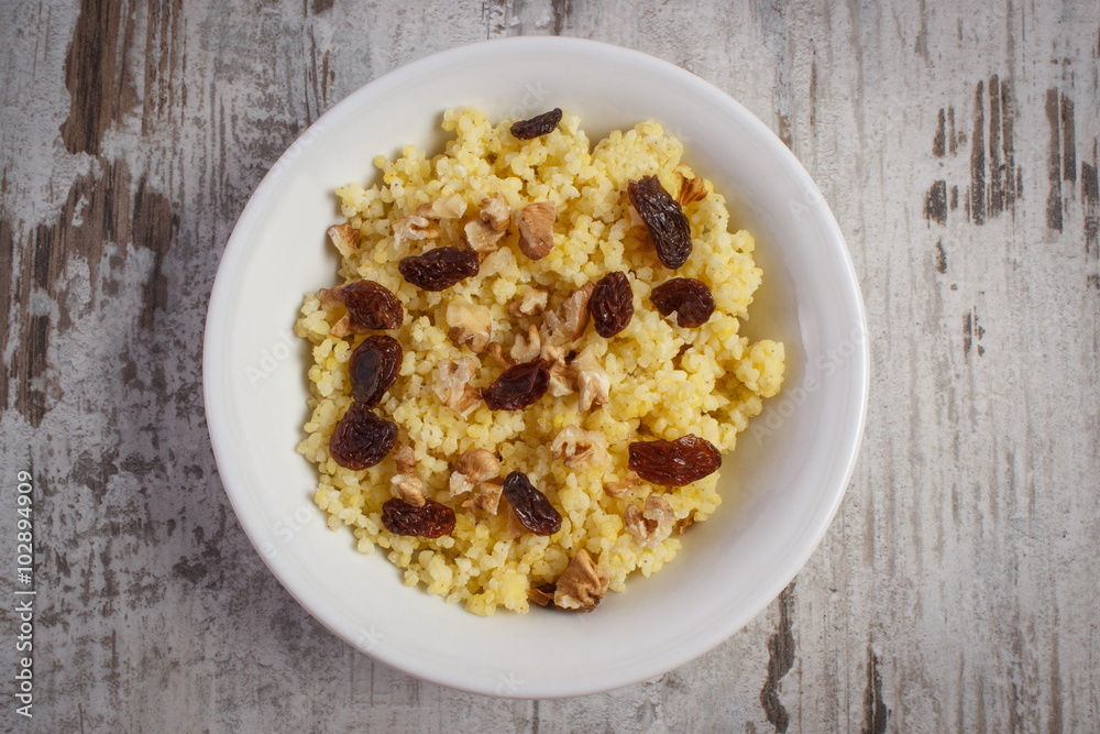 Cooked millet groats with raisins and walnuts on white plate, healthy food and nutrition Cooked millet groats with raisins and walnuts on white plate, healthy food and nutrition
