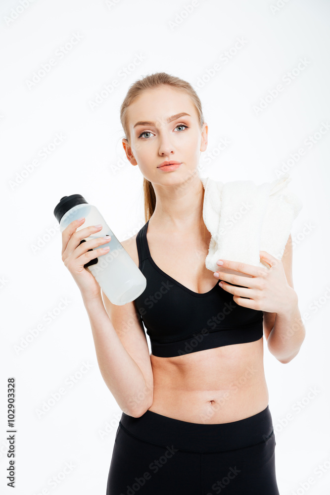 Confident sportswoman standing with bottle of water and white towel Confident sportswoman standing with bottle of water and white towel