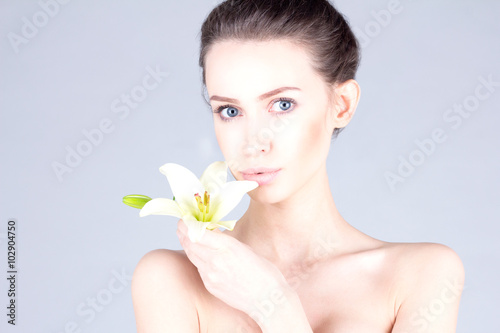 Beautiful young woman with a lily in her hands and with big blue eyes. SPA and beauty.