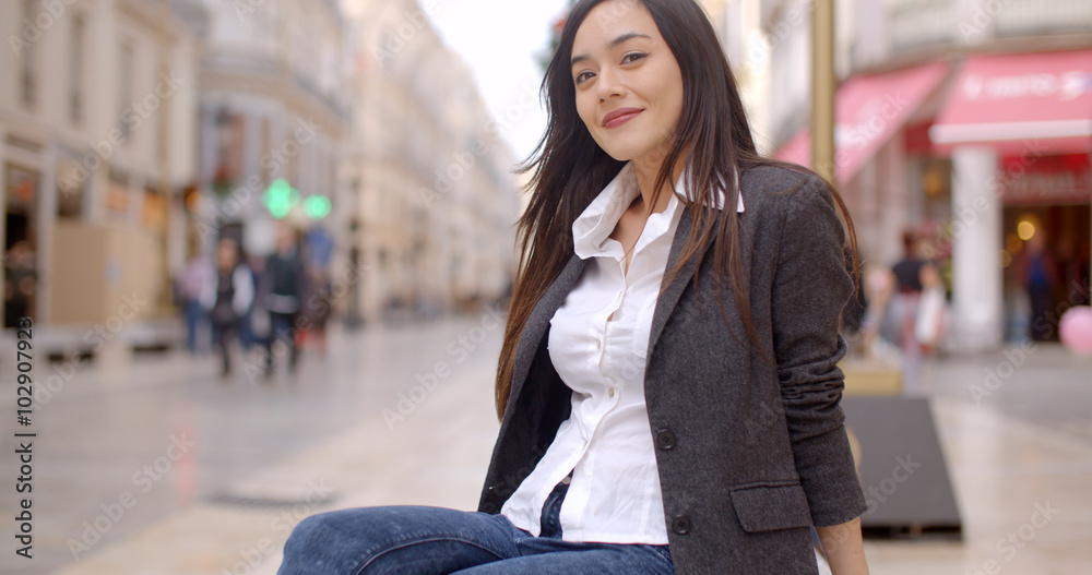 Fototapeta premium Relaxed attractive young woman sitting on a bench in town waiting for someone close up view with copy space