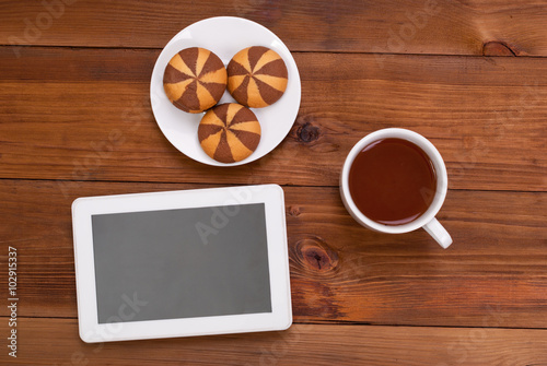 Cup of tea and cookies a digital tablet on the wooden table. Top view .