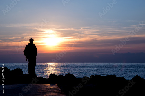 Silhouette of a man admiring winter sunset over italian sea - negative space on the right