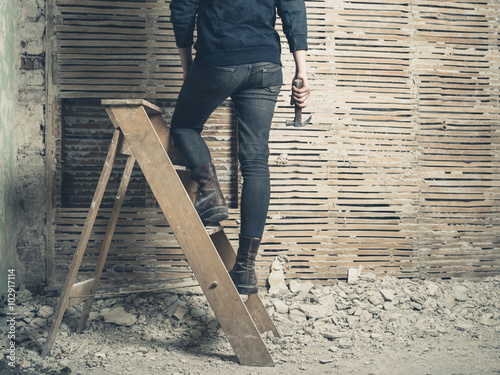 Woman standing on stepladder by wattle and daub wall