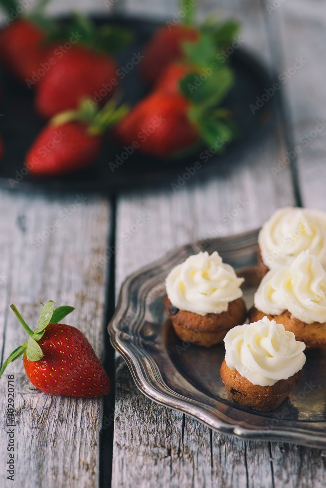 Still life with plate of strawberries and plate of cupcakes with cheese cream