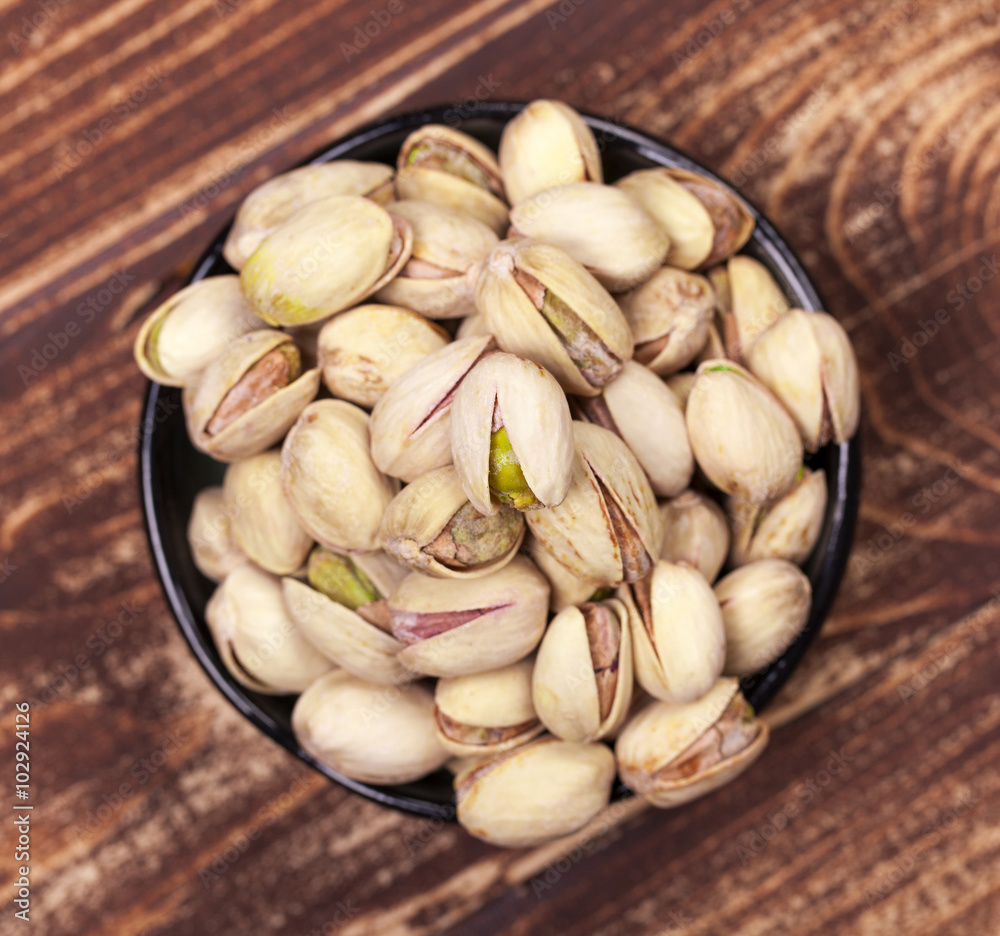 Black bowl of pistachios on aged wooden background Black bowl of pistachios on aged wooden background
