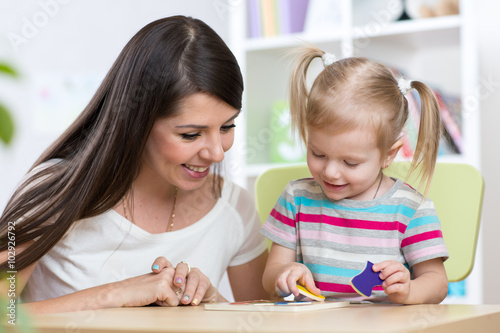 Little girl is solving puzzle. Mother watching at her actions