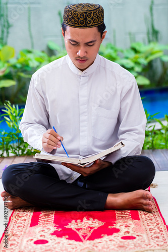 Asian Muslim man studying Koran or Quran photo