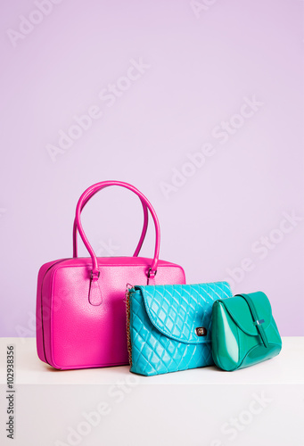 Three colorful leather bags and purses on the table. isolated on light purple color. 