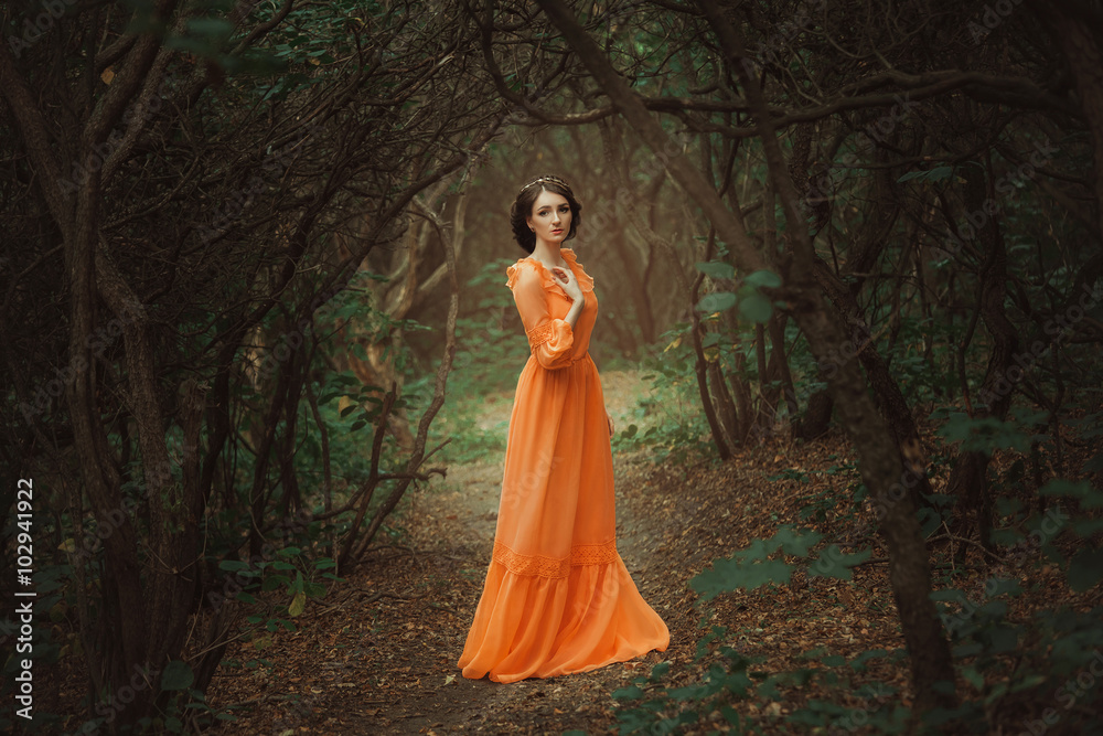 Fototapeta premium Piękna hrabina w długiej pomarańczowej sukience spaceruje po zielonym lesie pełnym gałęzi, elfka, księżniczka w sukience vintage, królowa lasu, modne stonowane kreatywne kolory komputerowe