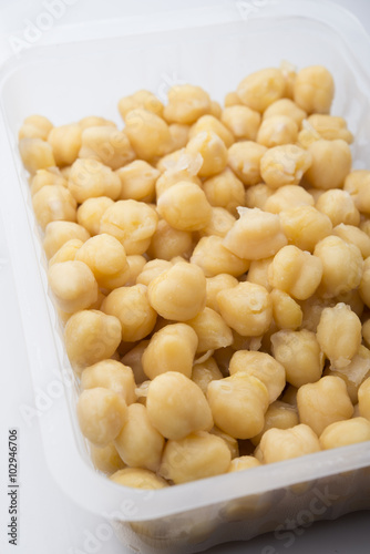 a plastic jar with cooked chickpeas on a white background