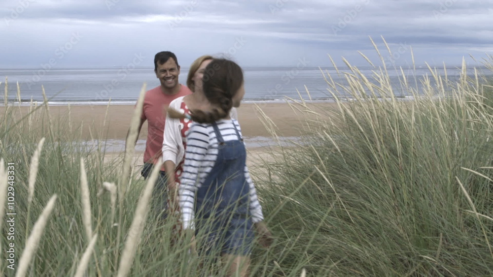 A family of four are leaving the beach together. The little boy is running ahead smiling and laughing. A family of four are leaving the beach together. The little boy is running ahead smiling and laughing.