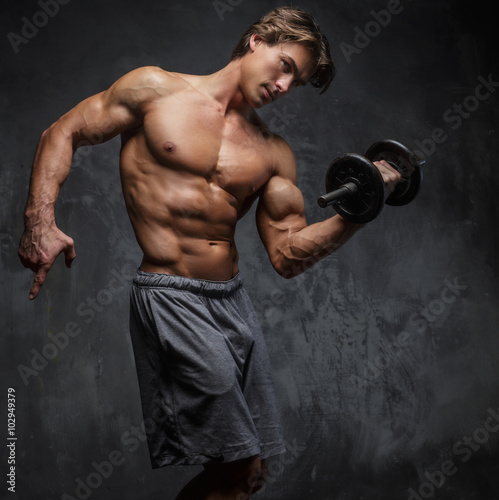 Shirtless muscular man holding a dumbbell.