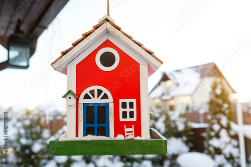 Wooden bird house of red color hanging outdoors in winter covered with snow