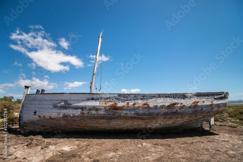 Abandoned boat on the vegetation on the sand dunes of Ria Formosa marshlands located in the Algarve, Portugal.