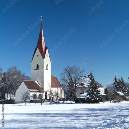Winter view of the church of Thoerl-Maglern (Pfarrkirche St. Andreas) with snow and the Alps in the background, Arnoldstein, Austria 