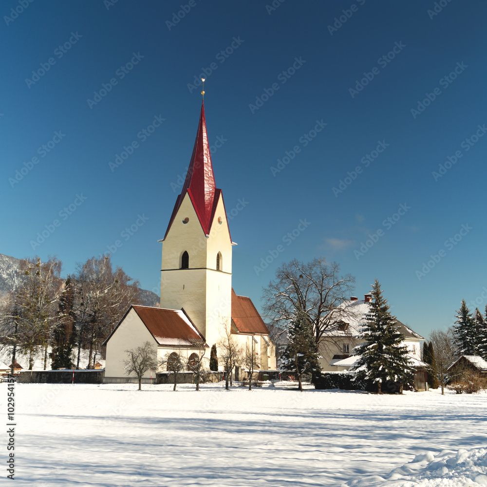 Winter view of the church of Thoerl-Maglern (Pfarrkirche St. Andreas) with snow and the  Alps in the background, Arnoldstein, Austria
