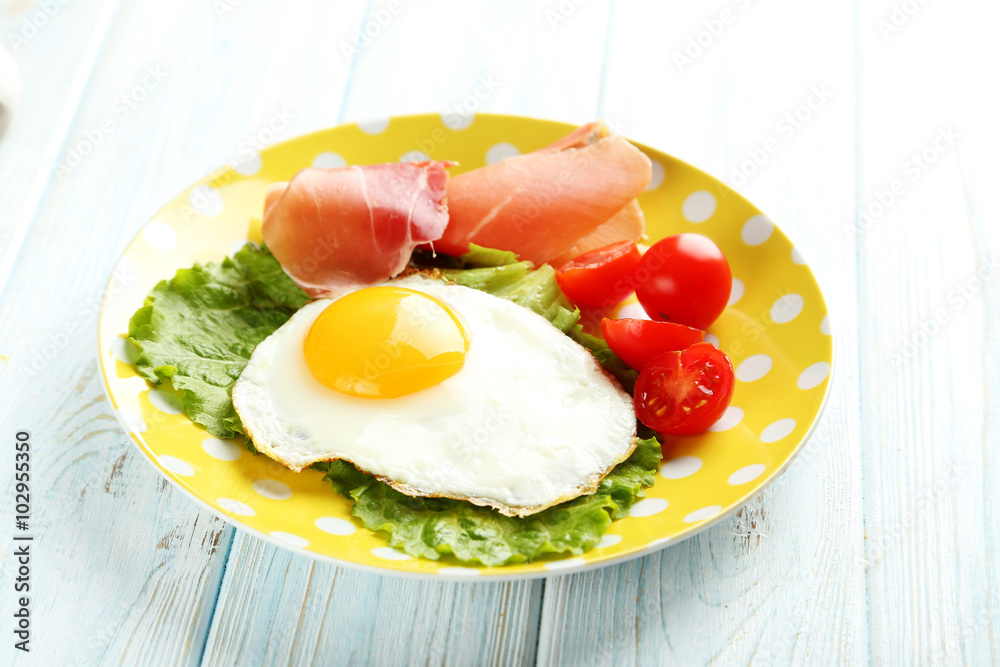 Fried eggs with bacon on plate on blue wooden table