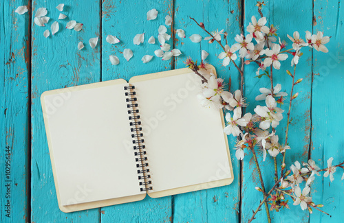 top view image of spring white cherry blossoms tree, open blank notebook on blue wooden table. vintage filtered and toned image
 photo