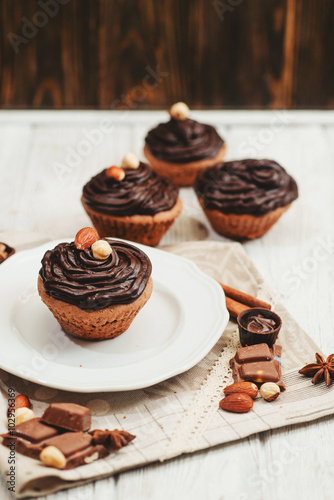  Chocolate cupcakes with cream , almonds , hazelnuts and cinnamon on a wooden background 