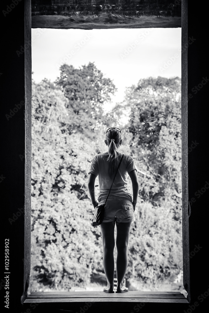 young woman standing on the edge of ancient window and looking at view  through it. Conceptual image for past and future