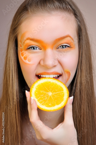 Young beautiful woman with creative orange makeup eating an orange