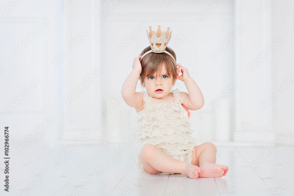 Fototapeta premium baby girl wearing a crown sitting on the white wood floor