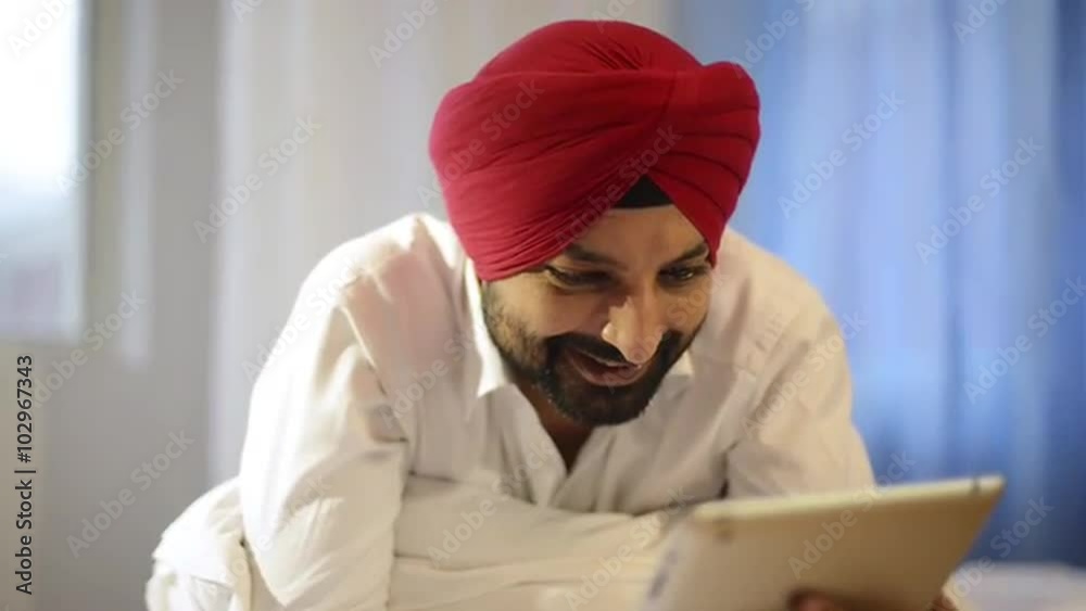 Tilt up shot Sikh man using a digital tablet and smiling Tilt up shot Sikh man using a digital tablet and smiling