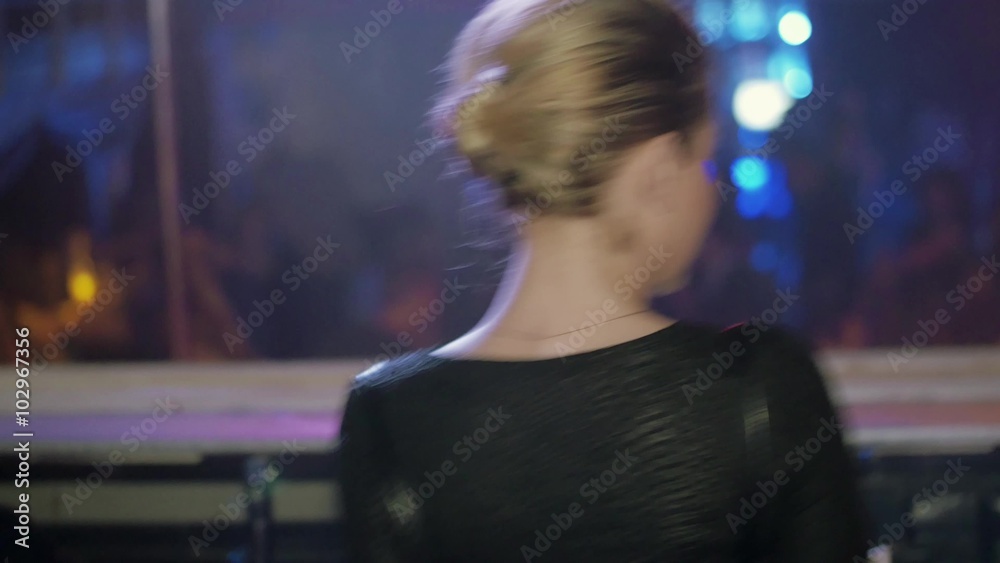 Back side of blonde Dj girl dance, shake shoulders at turntable in nightclub Back side of blonde Dj girl dance, shake shoulders at turntable in nightclub