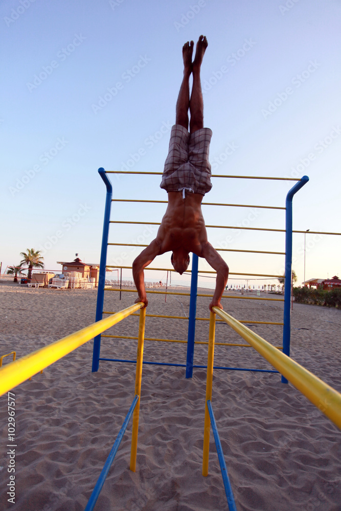 Fototapeta premium Man showing impressive strength, doing a handstand in beach. 