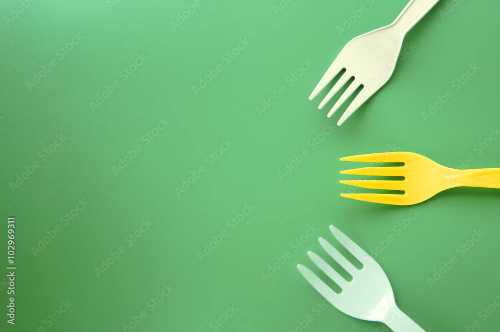 White and yellow plastic forks appearing to come together on a green background White and yellow plastic forks appearing to come together on a green background