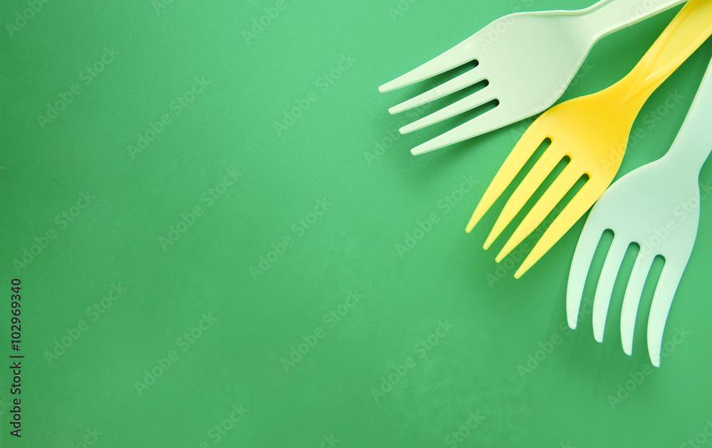 White and yellow plastic forks arranged in a corner of a green background White and yellow plastic forks arranged in a corner of a green background