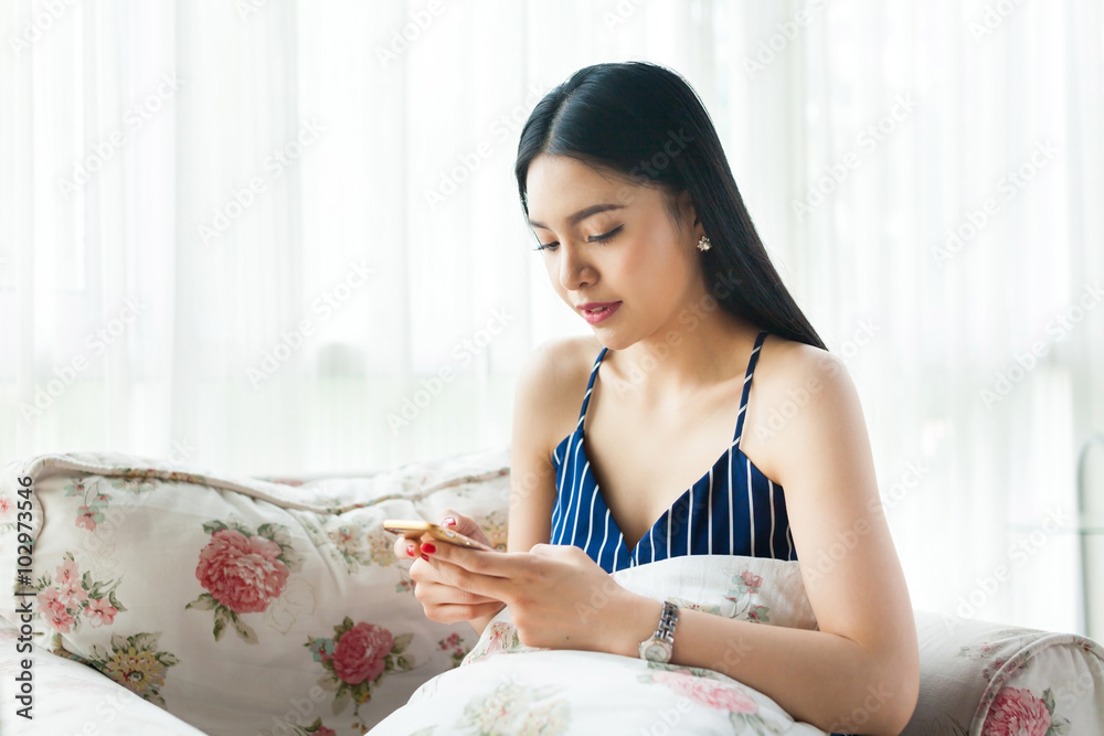 Asian woman playing her phone on a cozy sofa Asian woman playing her phone on a cozy sofa